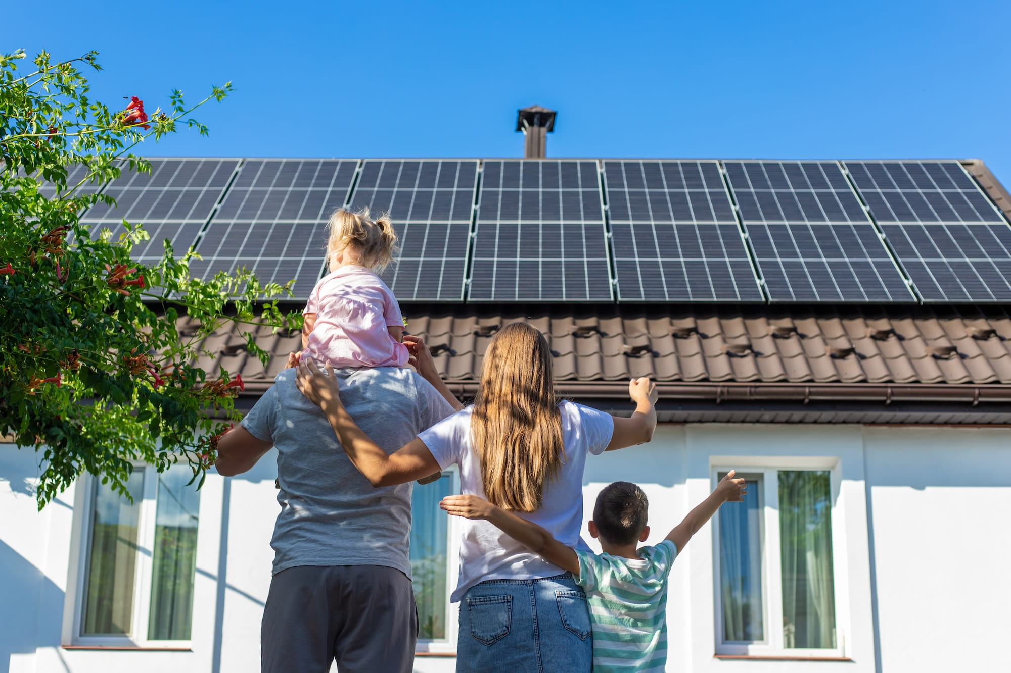 Familie vor ihrem Eigenheim mit Photovoltaik-Anlage